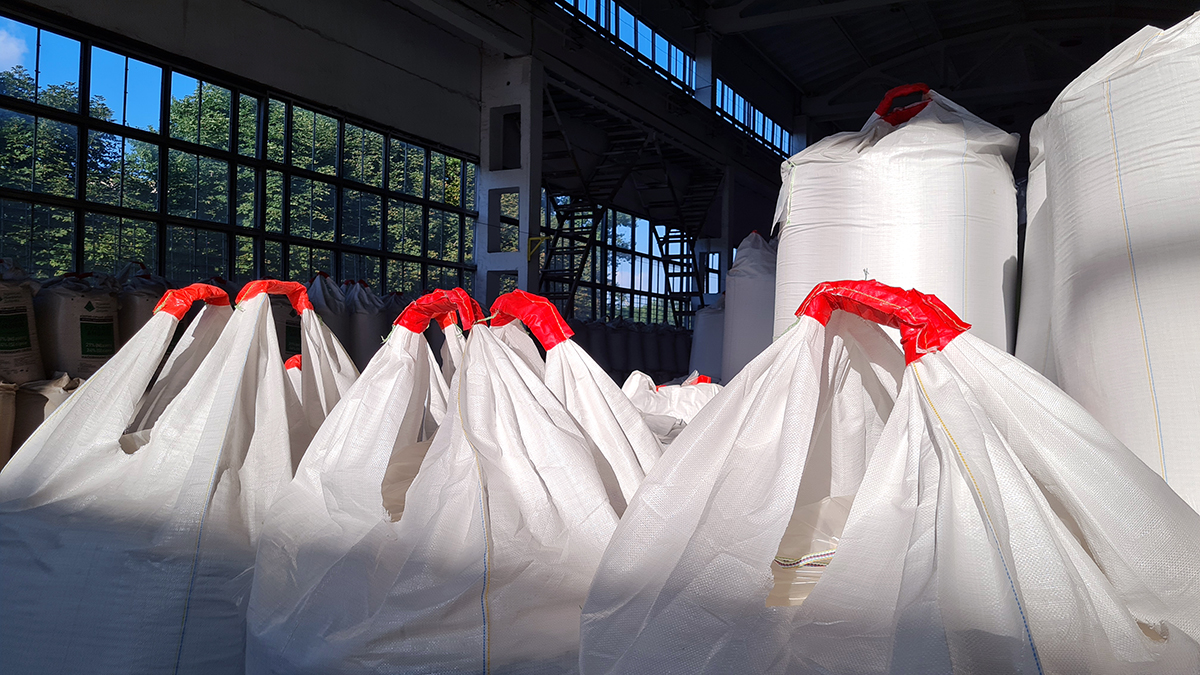 Group of white jumbo-bags with chemical fertilizers into a warehouse.